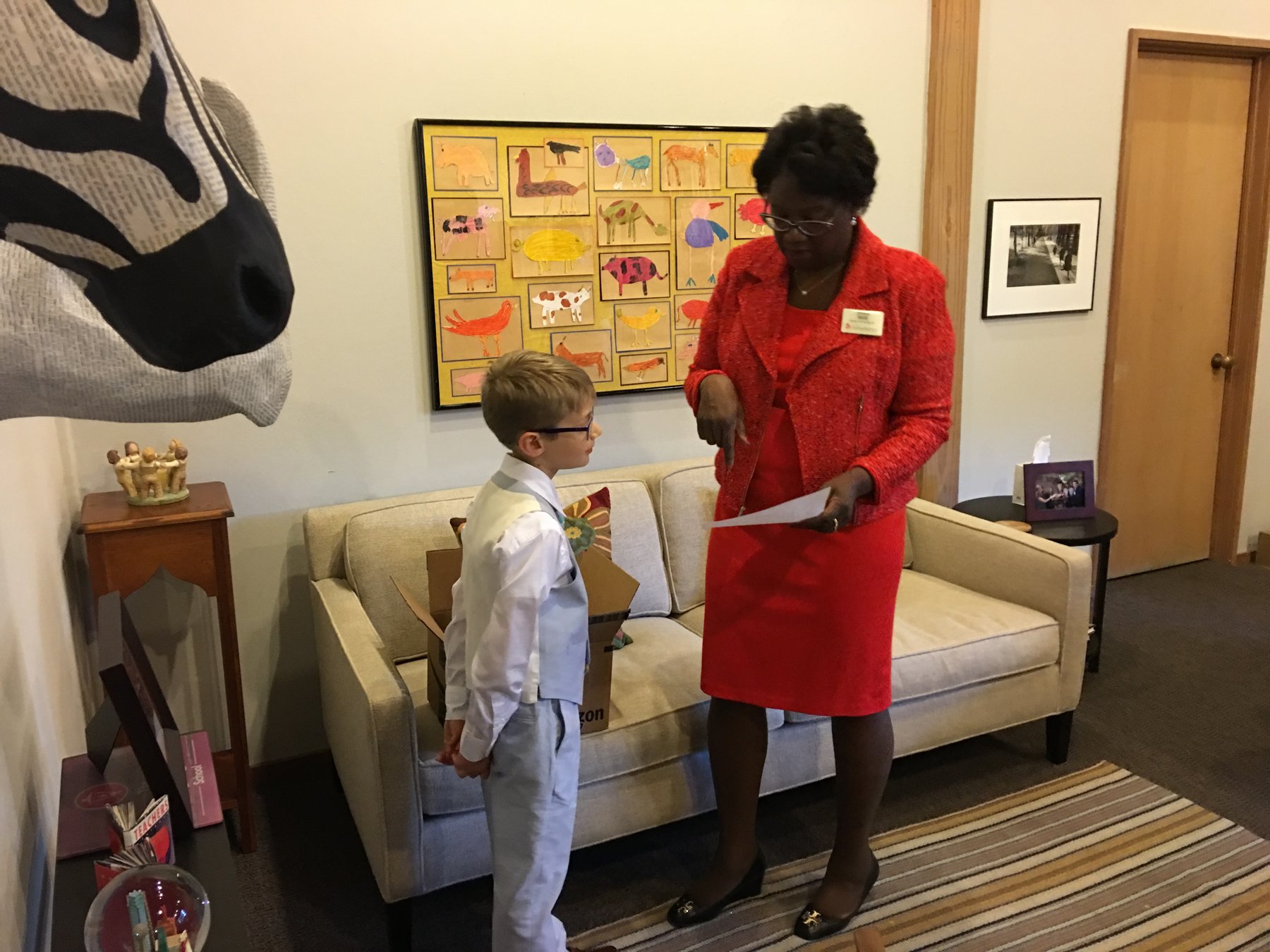 Andrew Hillman. Ashton Hillman, formal with glasses and light blue vest, with a school official in red in an office during Head of School for the Day.